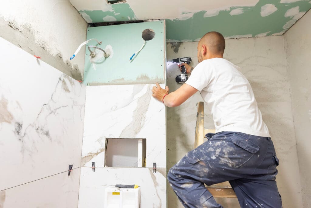 Plumber using electric screwdriver. Bathroom renovation concept. Marble ceramic tiles with spacers and grey cement walls in bathroom. Industrial builder working in toilet